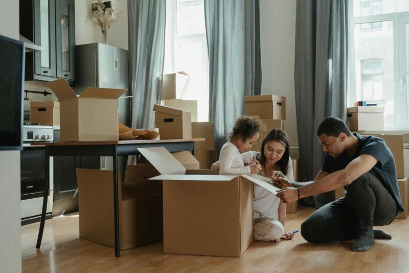 gezin zit op de grond in een woonkamer tussen verhuisdozen